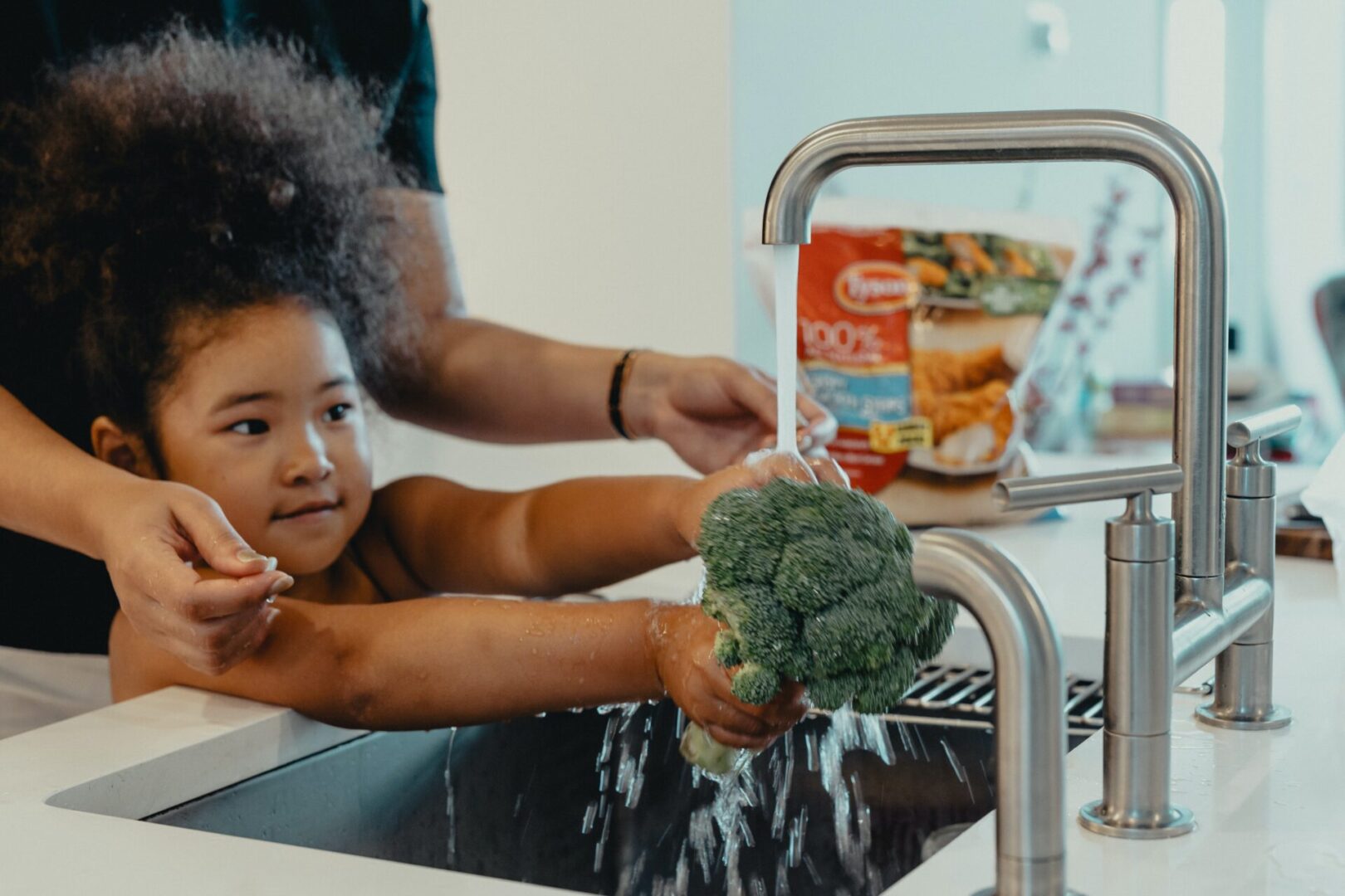 A child is washing broccoli in the sink.